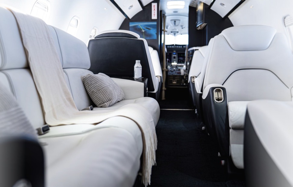White leather cabin of a midsize private jet with a cream throw and cushion